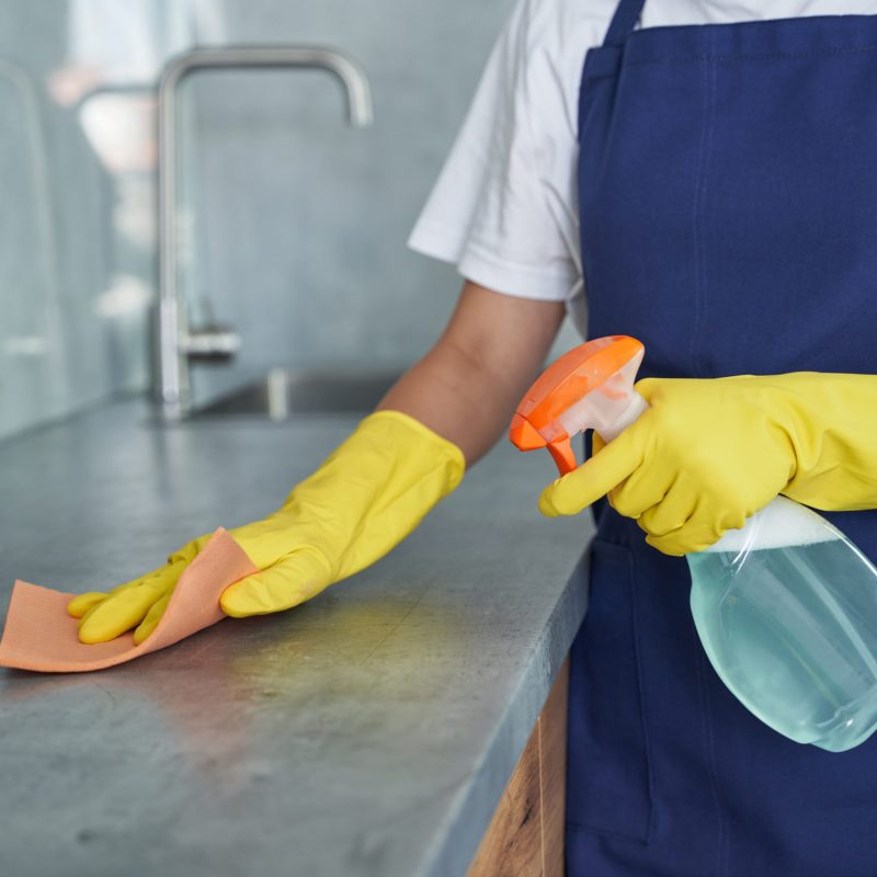 Cropped shot of young woman, cleaning lady cleaning the kitchen spraying the surfaces with detergent from a spray bottle. Housework and housekeeping, cleaning service concept